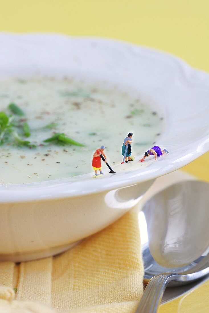 Miniature cleaning ladies scrubbing edge of plate of leek soup