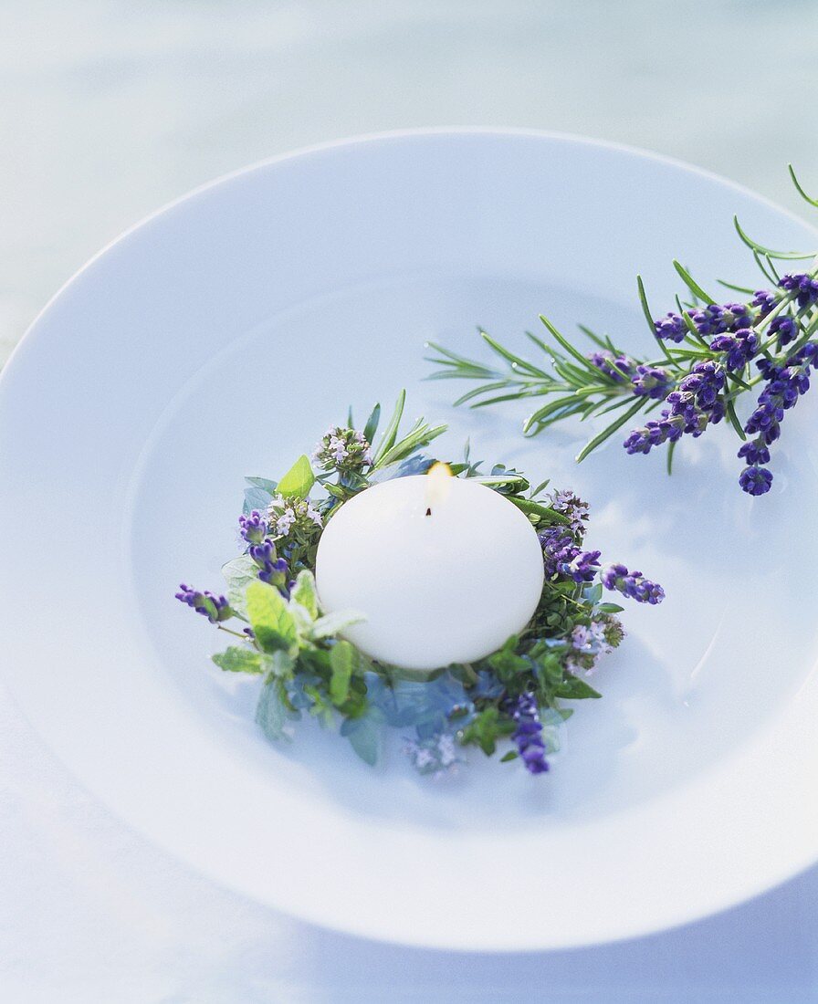 Lighted floating candle with ring of herbs on a plate