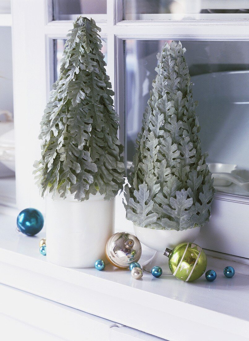 Small Christmas trees with baubles on a window-sill