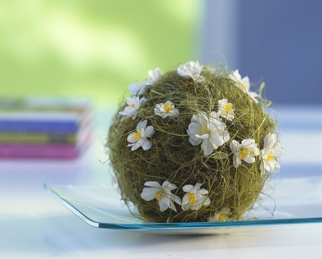 Dekokugel mit weissen Seidenblüten auf einem Glasteller