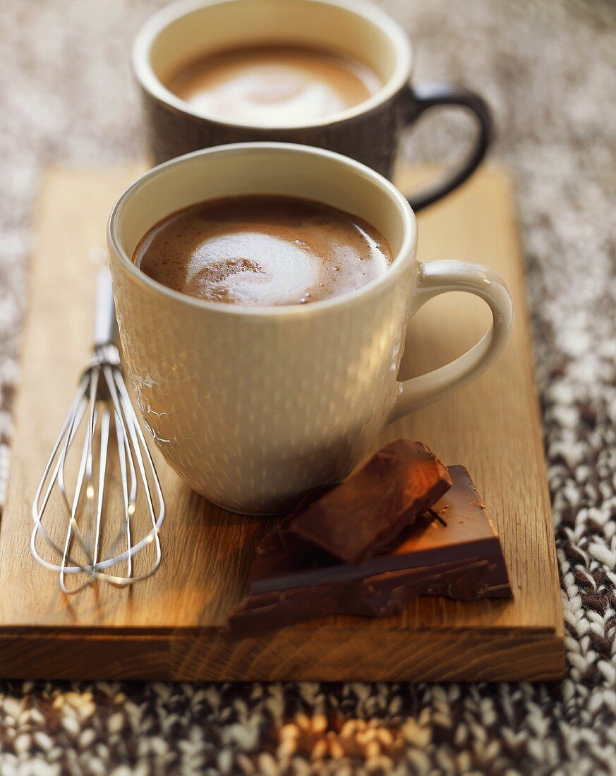Two mugs of hot chocolate on a wooden board
