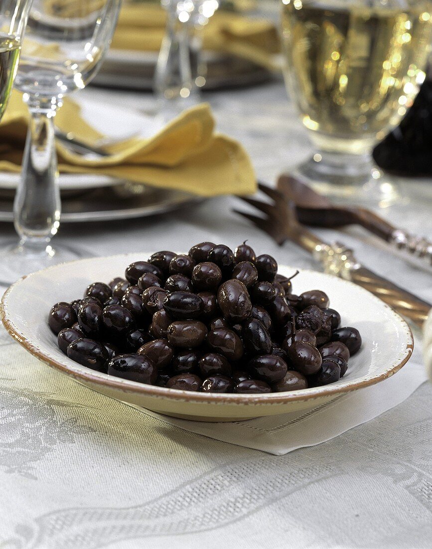 Schwarze Oliven auf Teller am gedeckten Tisch