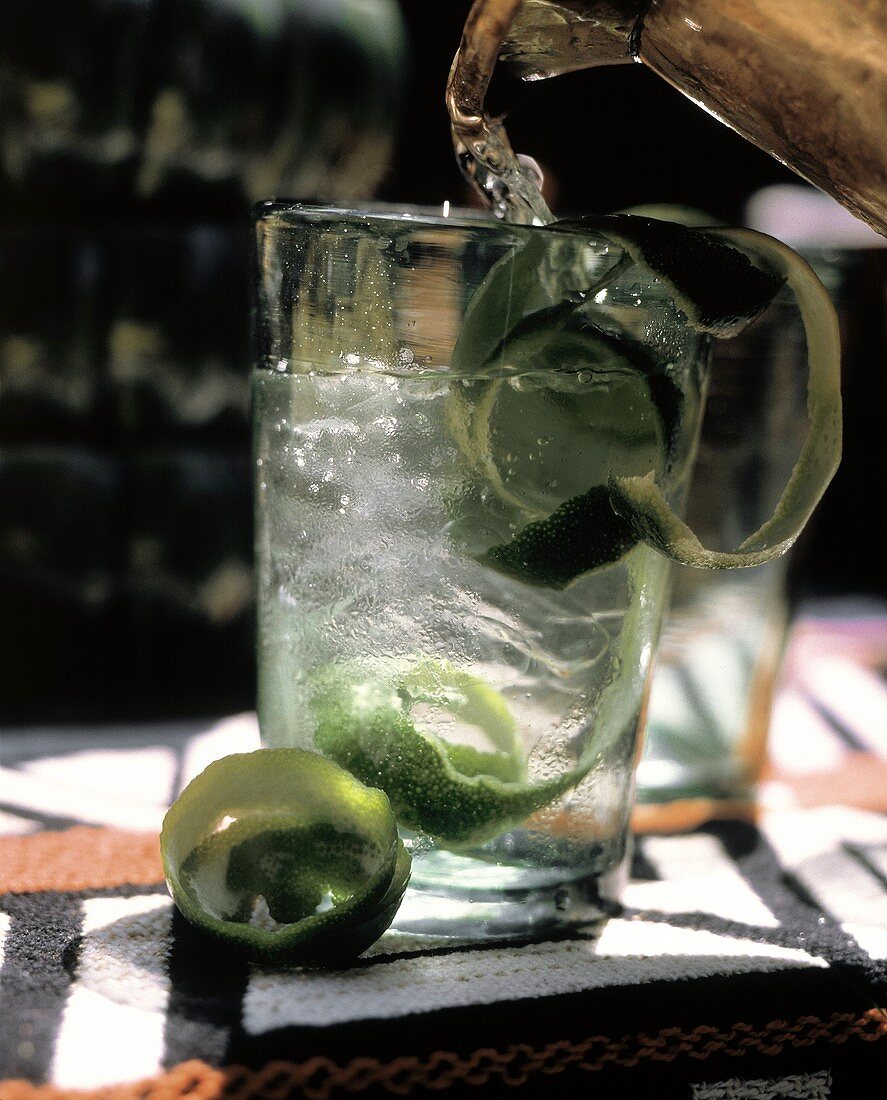 Wasser aus Krug in Glas mit Limettenscheiben gießen