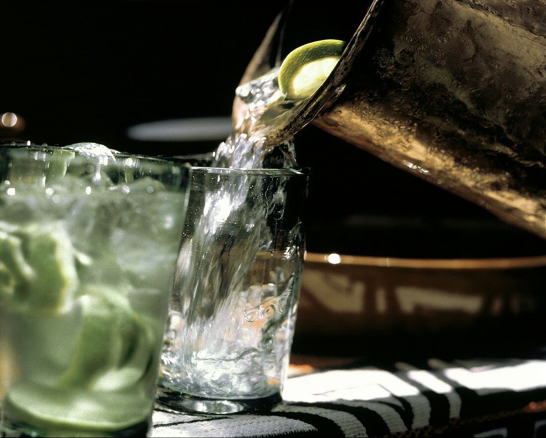 Wasser mit Limettenscheiben aus Krug in Glas gießen