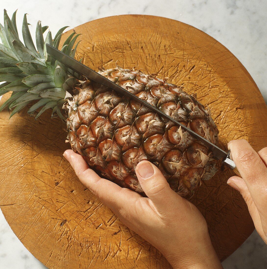 Cutting through a whole pineapple on a wooden plate