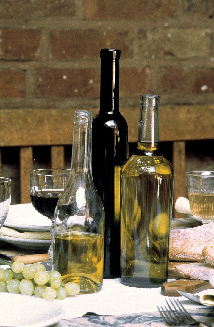 Weinflaschen, Weingläser, Brot & Trauben auf gedecktem Tisch