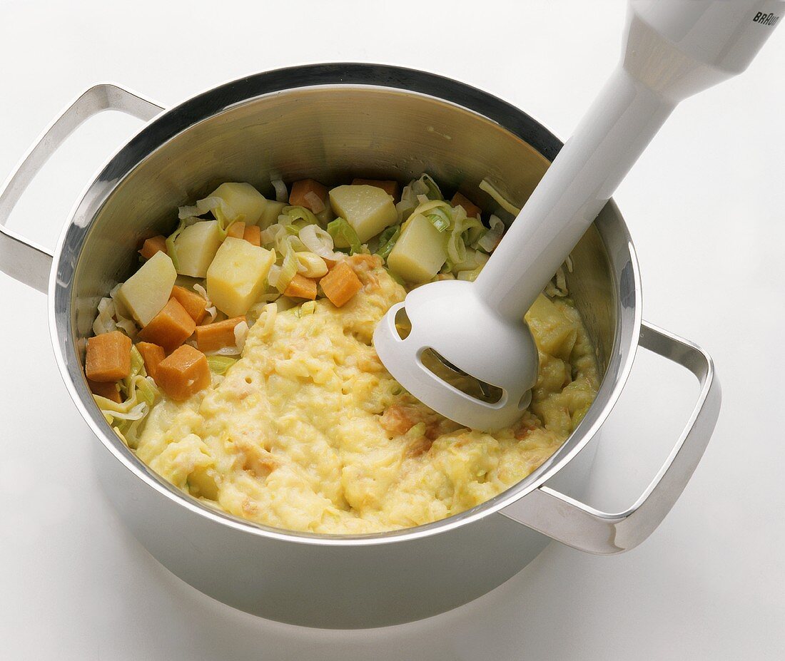 Chopping soup vegetables in pan with hand blender