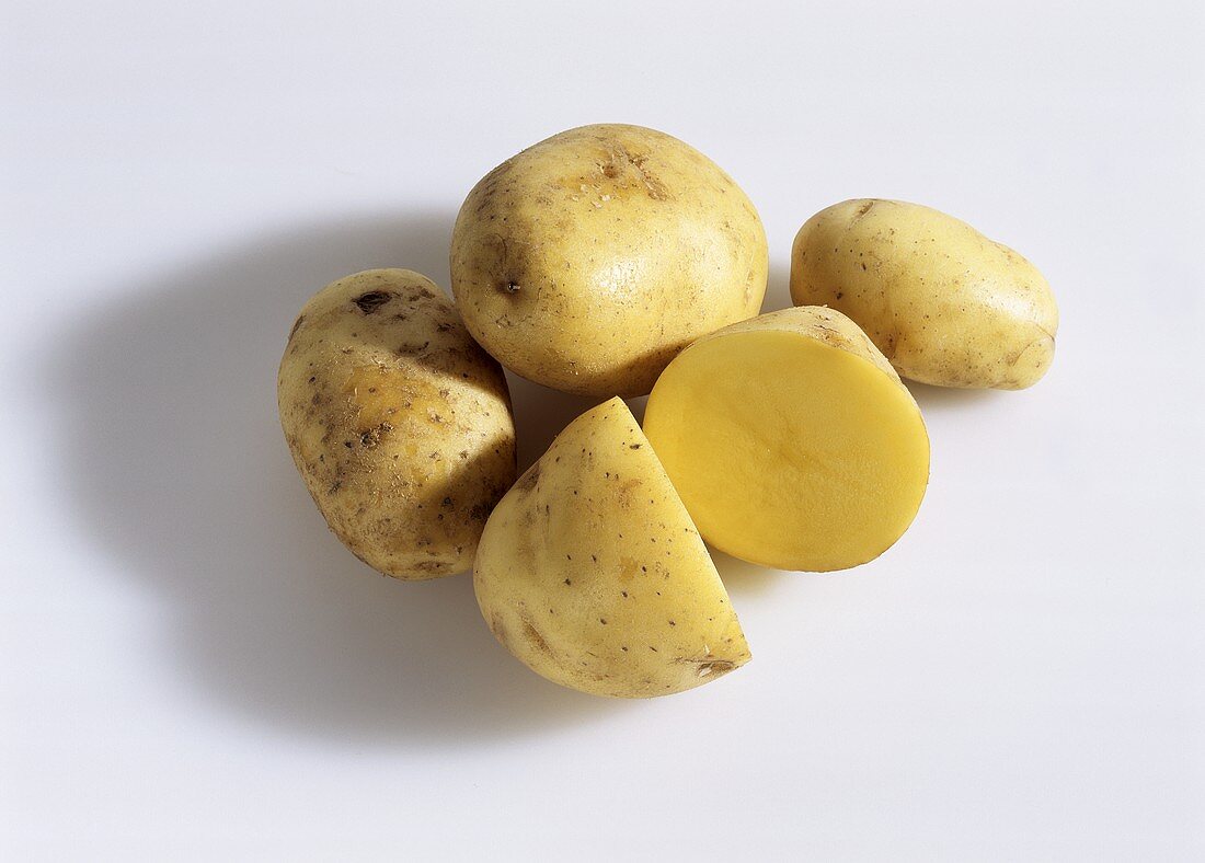 Mehrere Kartoffeln, eine davon in zwei Hälften geschnitten