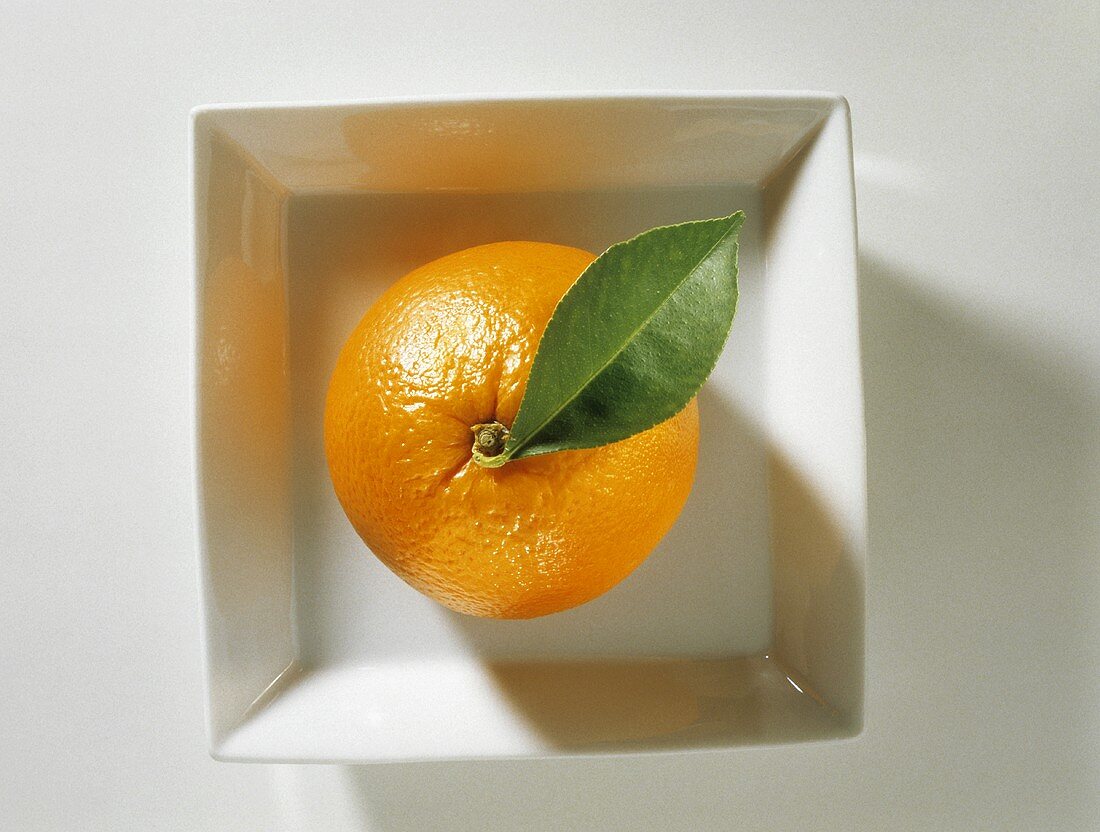 Orange mit Blatt in weißem Schälchen
