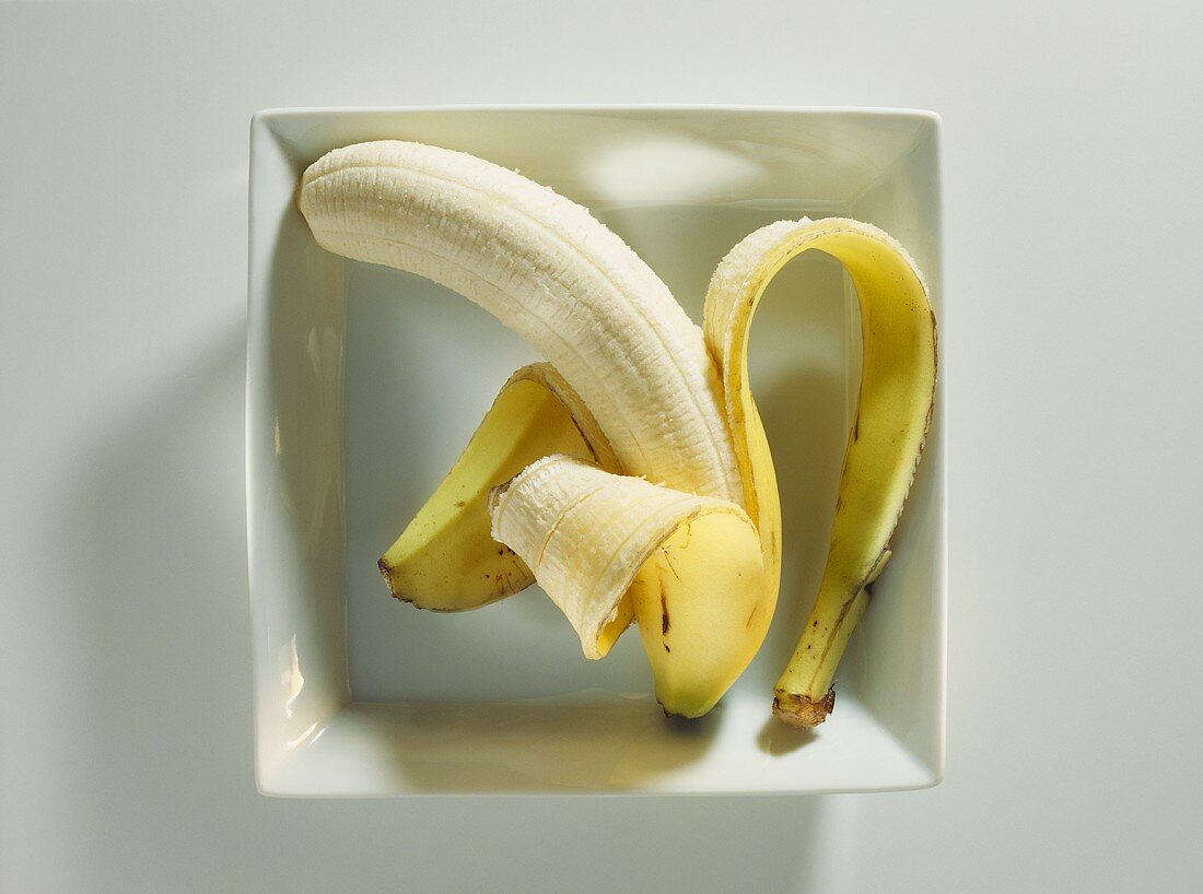 Eine Banane, halb geschält, in weißem Schälchen