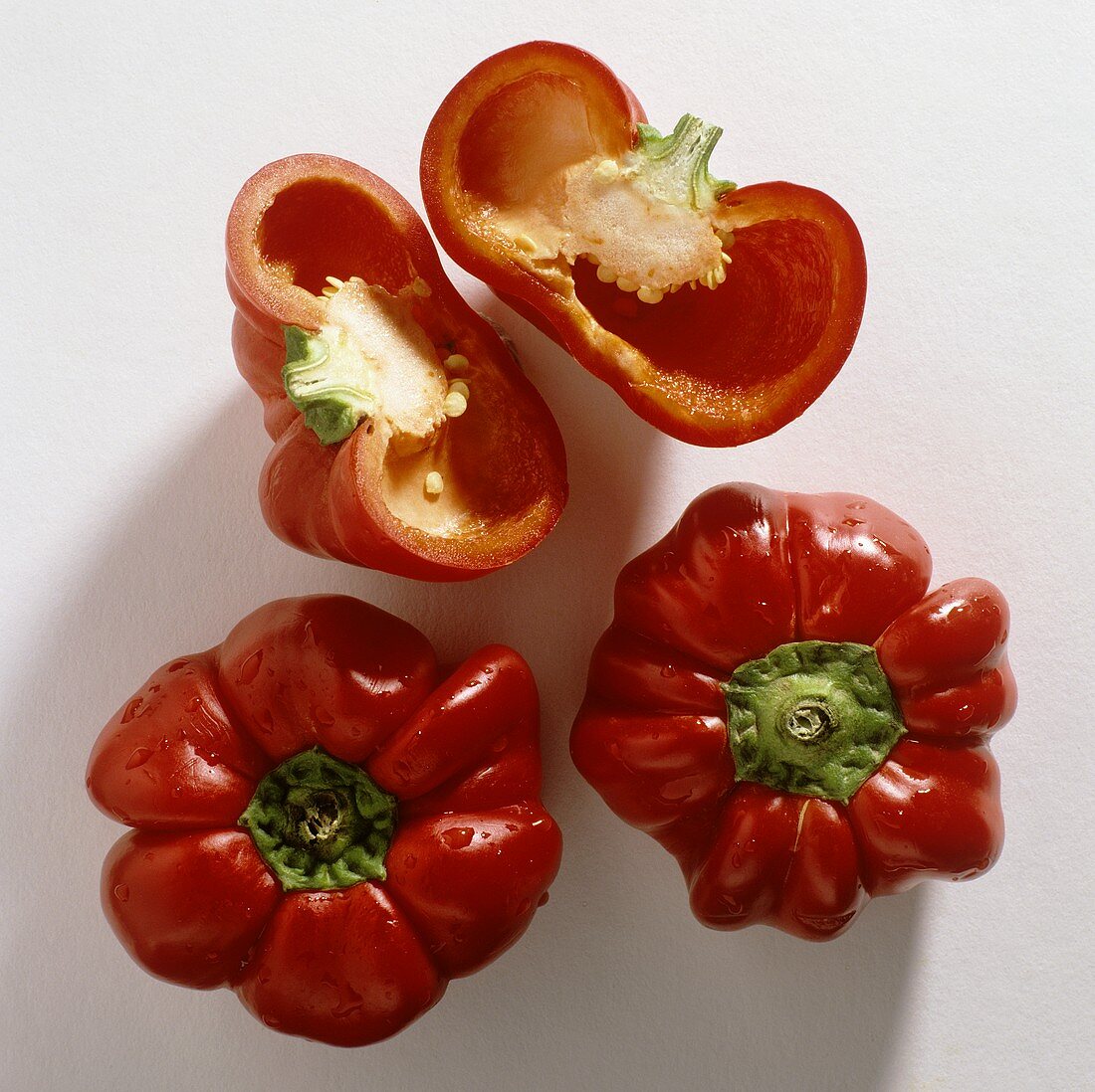 Three red peppers (bell peppers), one halved