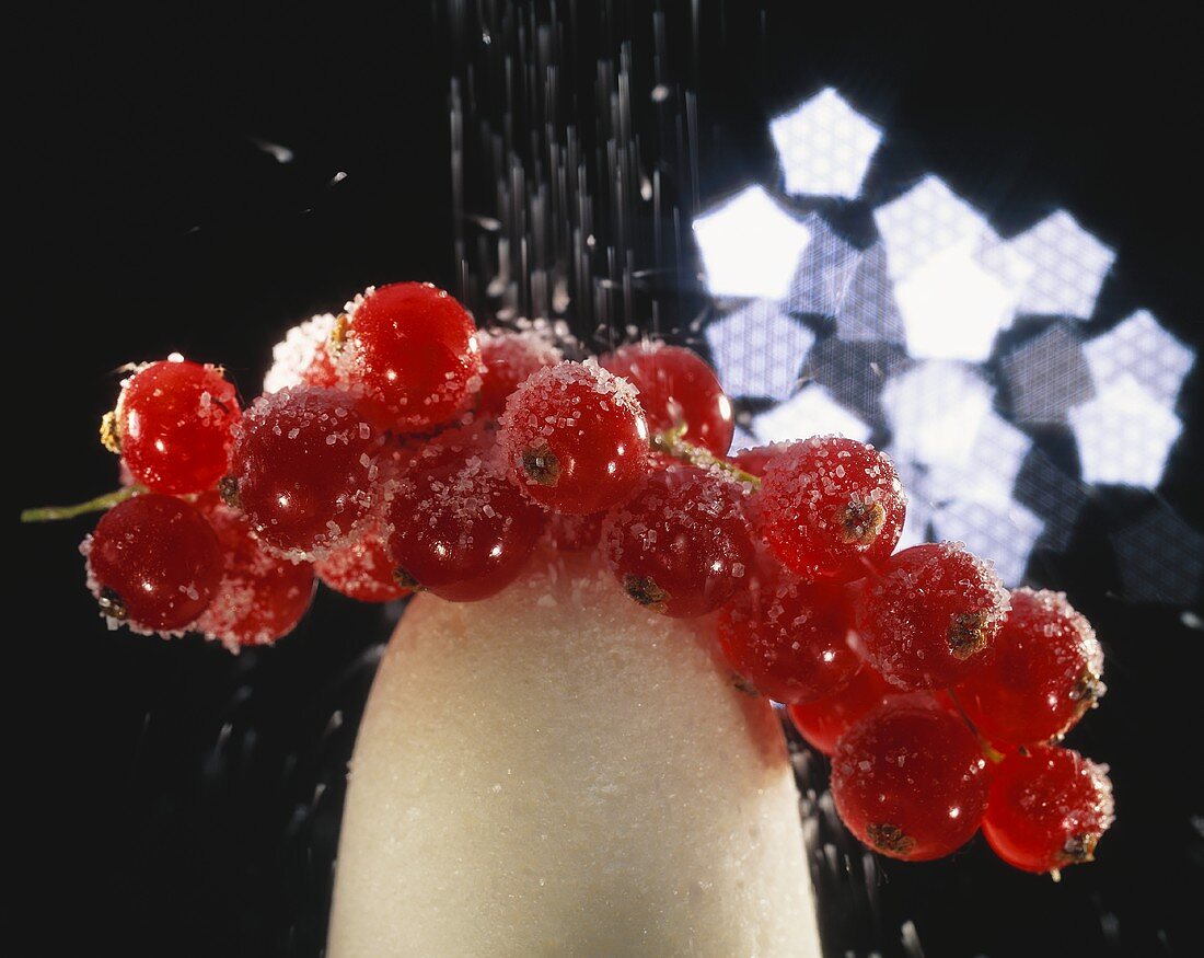 Zucker rieselt auf rote Johannisbeeren auf einem Zuckerhut