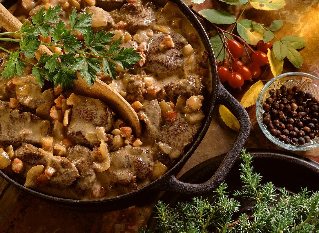 Wildschweinragout in gußeisernem Topf mit Holzlöffel