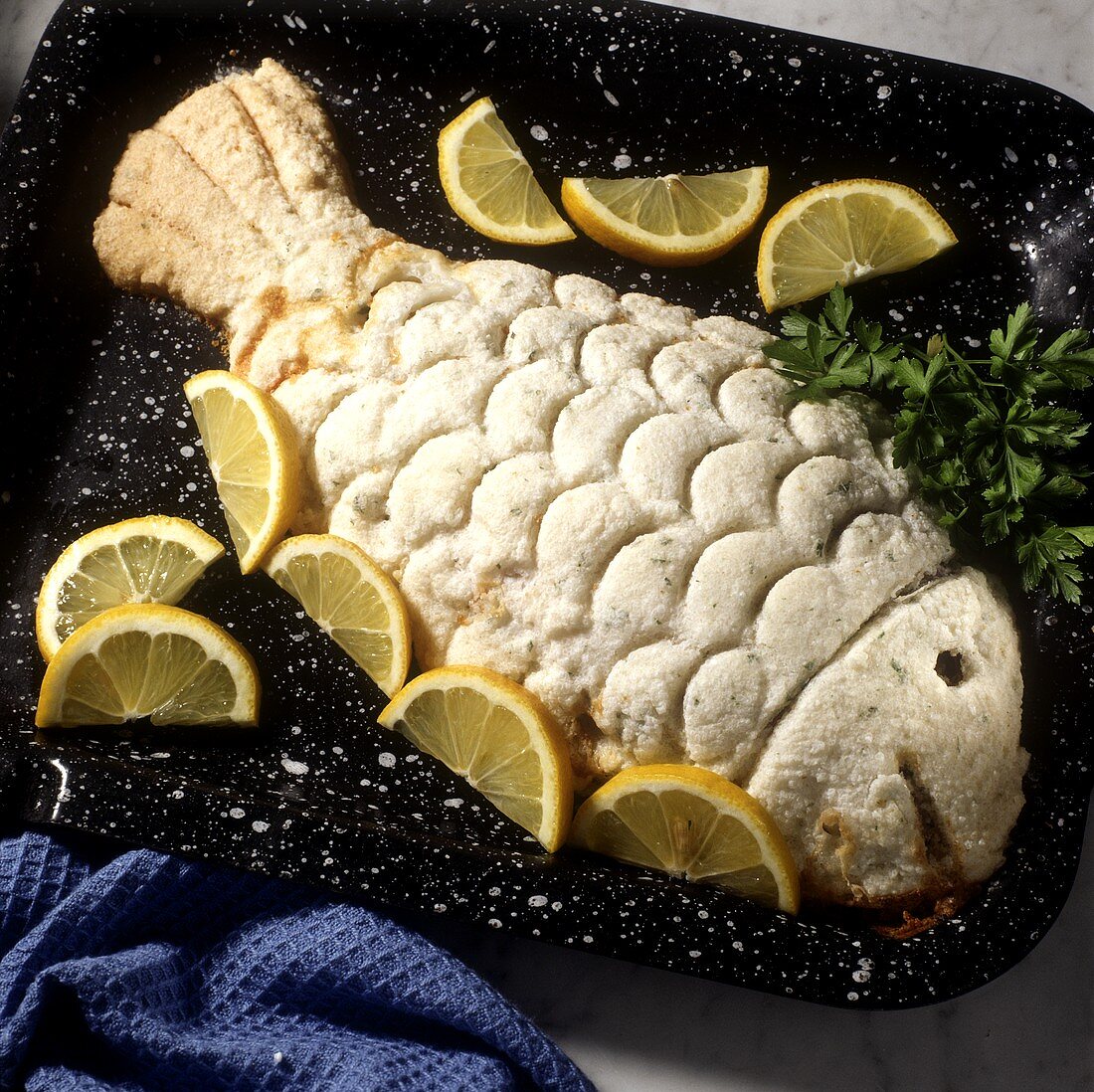Fish in salt crust with lemon wedges on baking tray