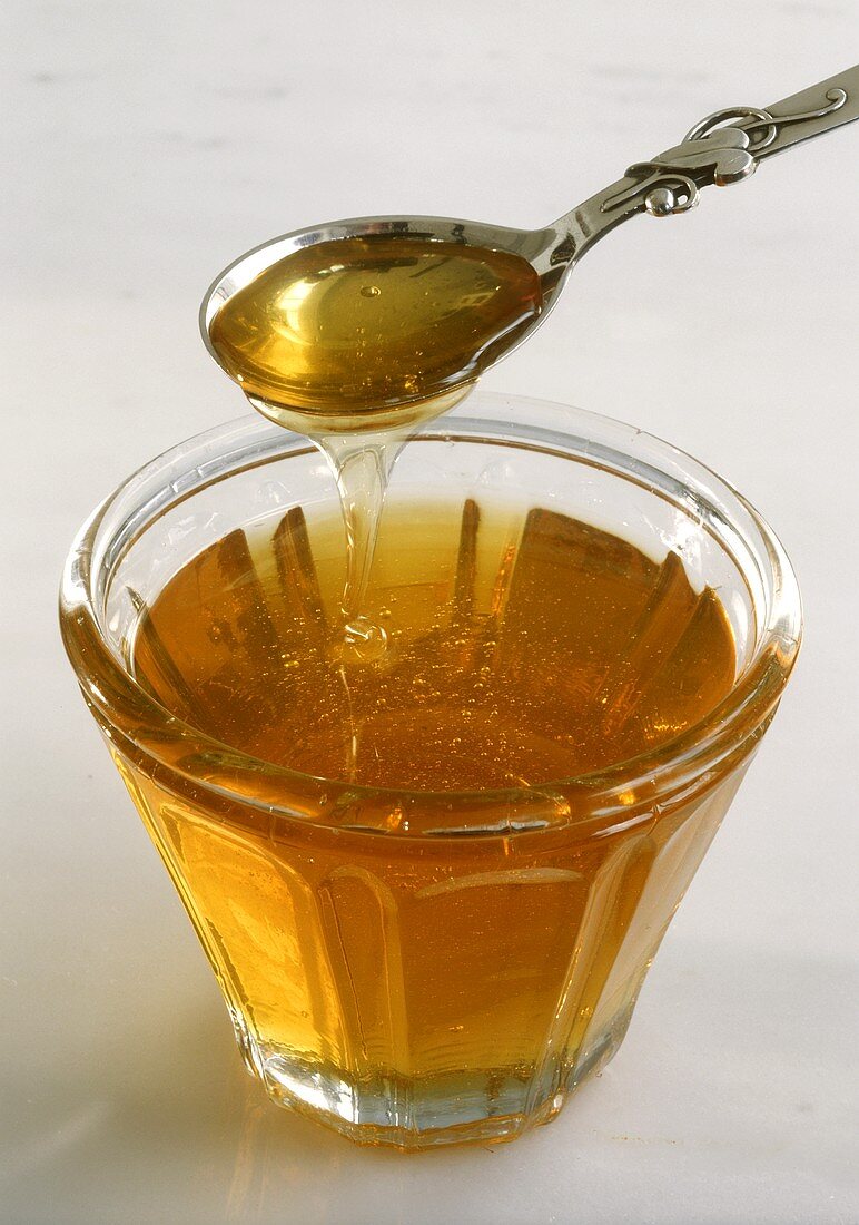 Honey Pouring From a Spoon into a Cup