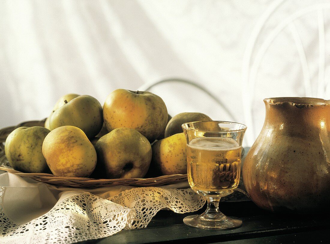 Ein Glas mit perlendem Cidre, mehrere Äpfel & Keramikkrug