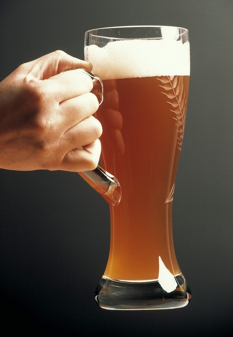 A Hand Holding a Tall Glass of Wheat Beer
