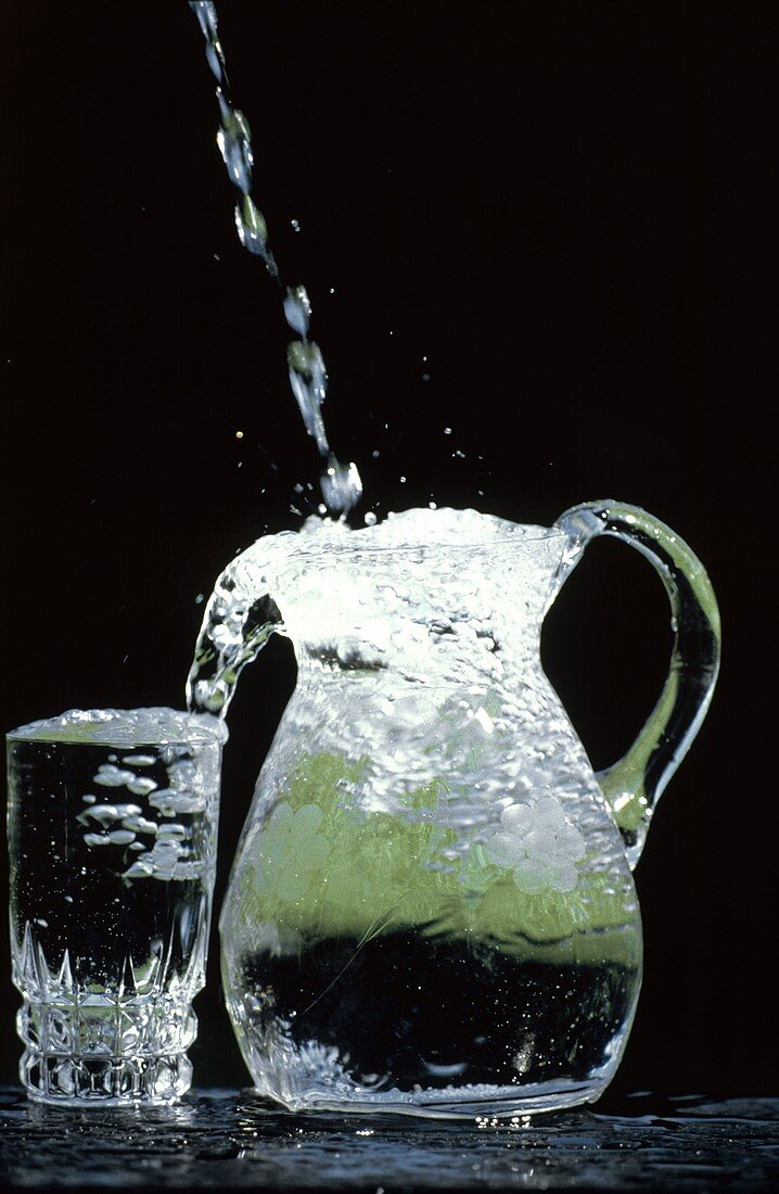 Wasser fliesst in eine Kanne & Trinkglas