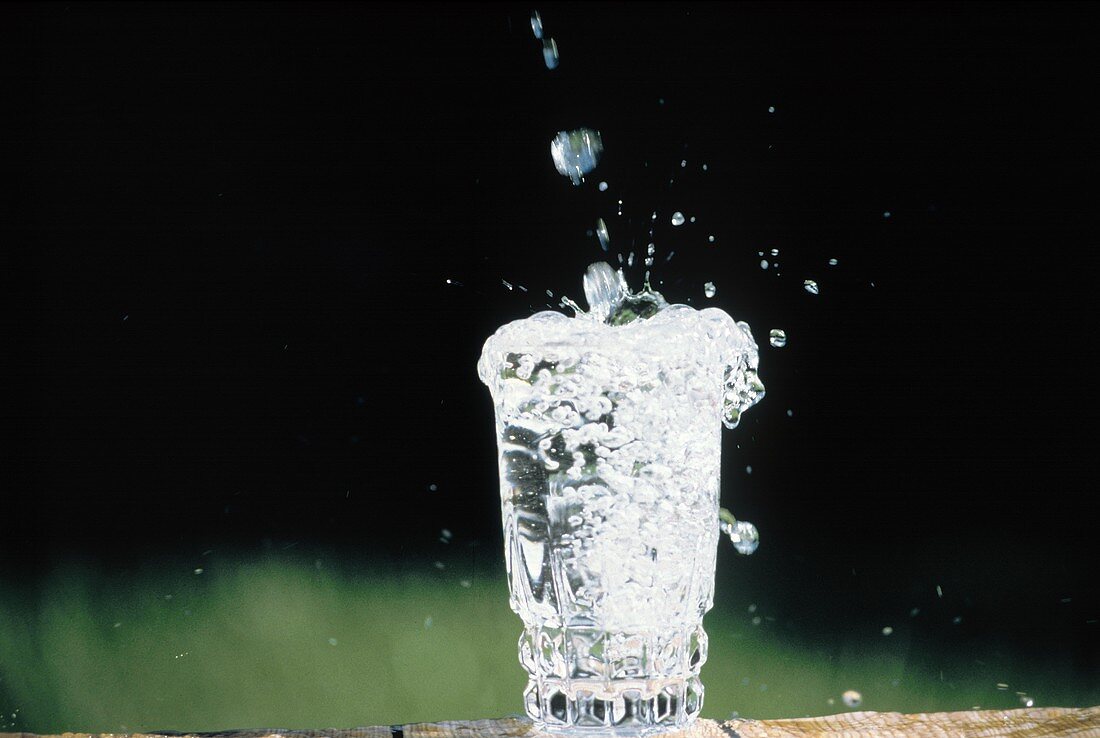 Wasser tropft in ein volles Wasserglas