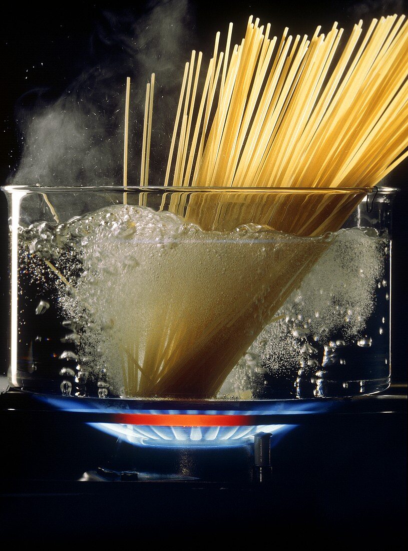 Spaghetti in Glastopf mit kochendem Wasser auf Gasflamme
