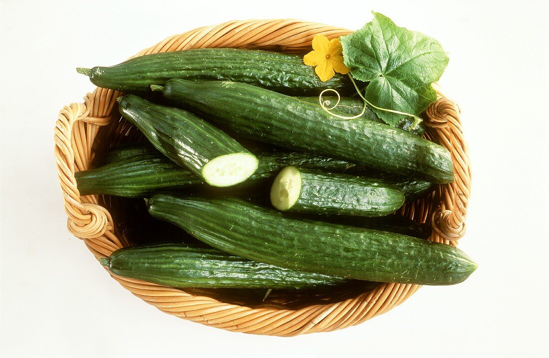 Several cucumbers in a basket with leaf and flower