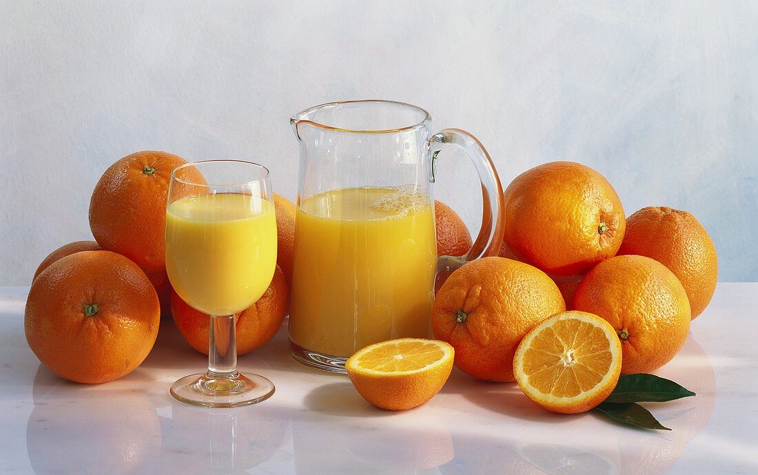 Orange Juice in a Glass and Pitcher; Surrounded by Fresh Oranges