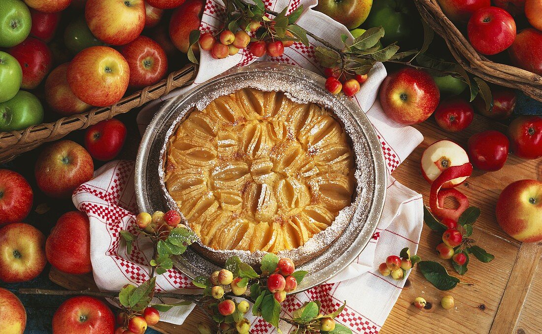 Turned-out apple tart with icing sugar and baskets of apples