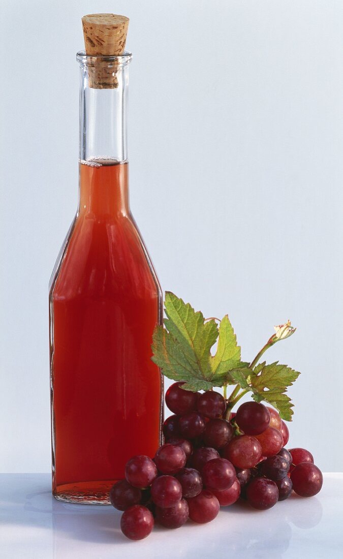 A bottle of grape vinegar, beside red grapes