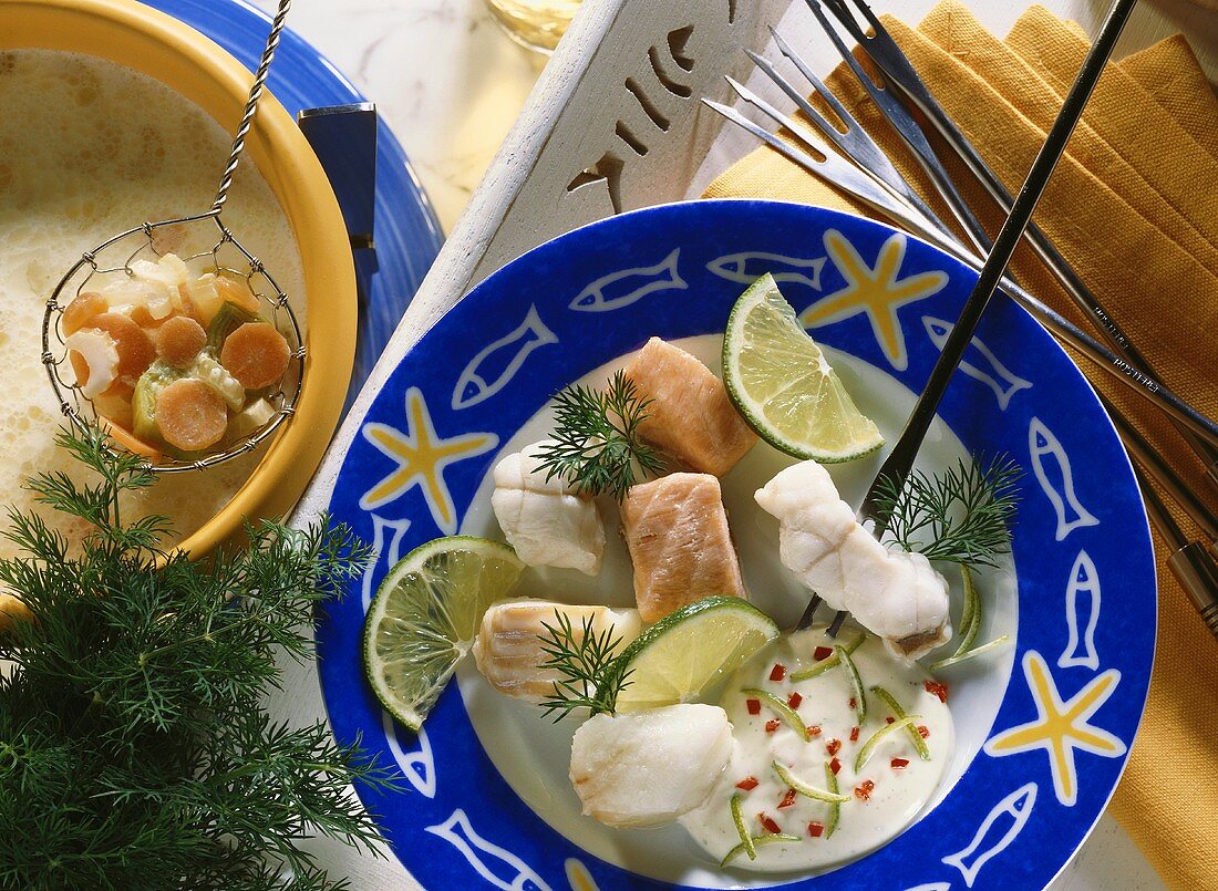 Edelfisch-Fondue mit Sahnefond auf Teller und Gemüse im Sieb