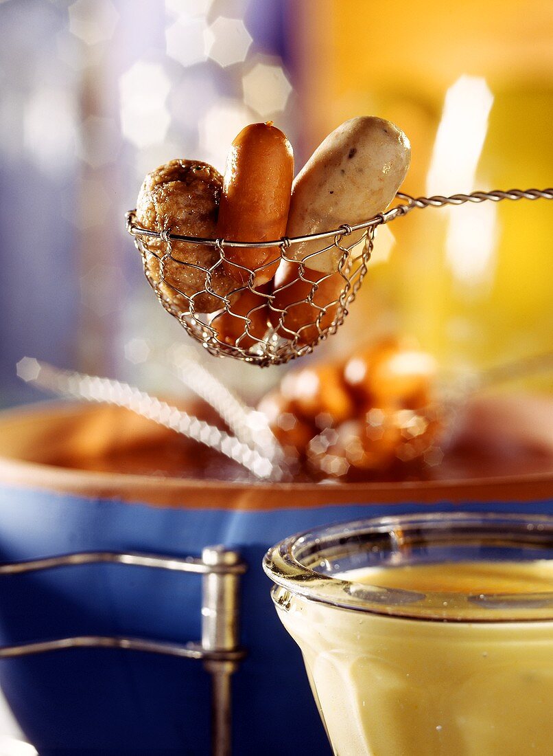 Sausage fondue, frikadeller in slotted spoon over fondue pot