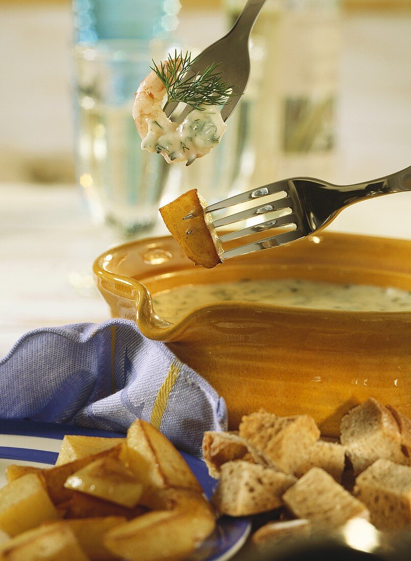 Käse-Dill-Fondue mit Garnele, Kartoffel auf Gabeln überm Topf