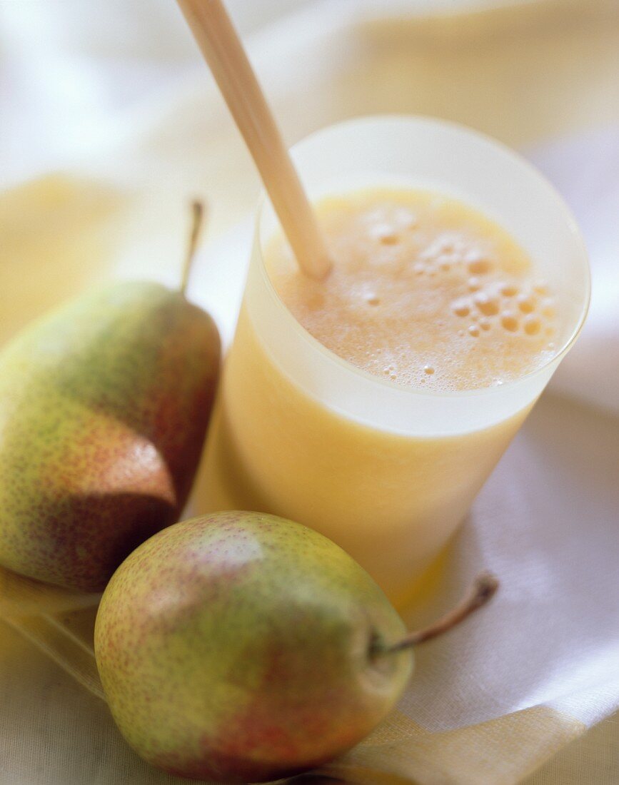 Pear & orange drink in glass, two fresh pears beside it