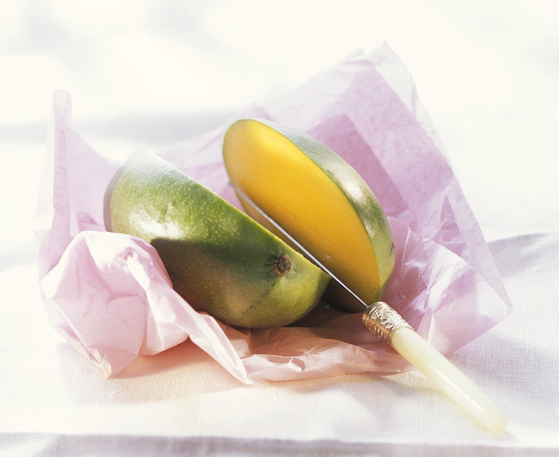 Mango on pink paper, cut into two halves, & knife