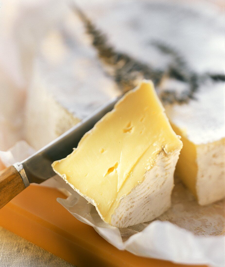Ein Stück Weichkäse mit Messer vor angeschnittenem Käse