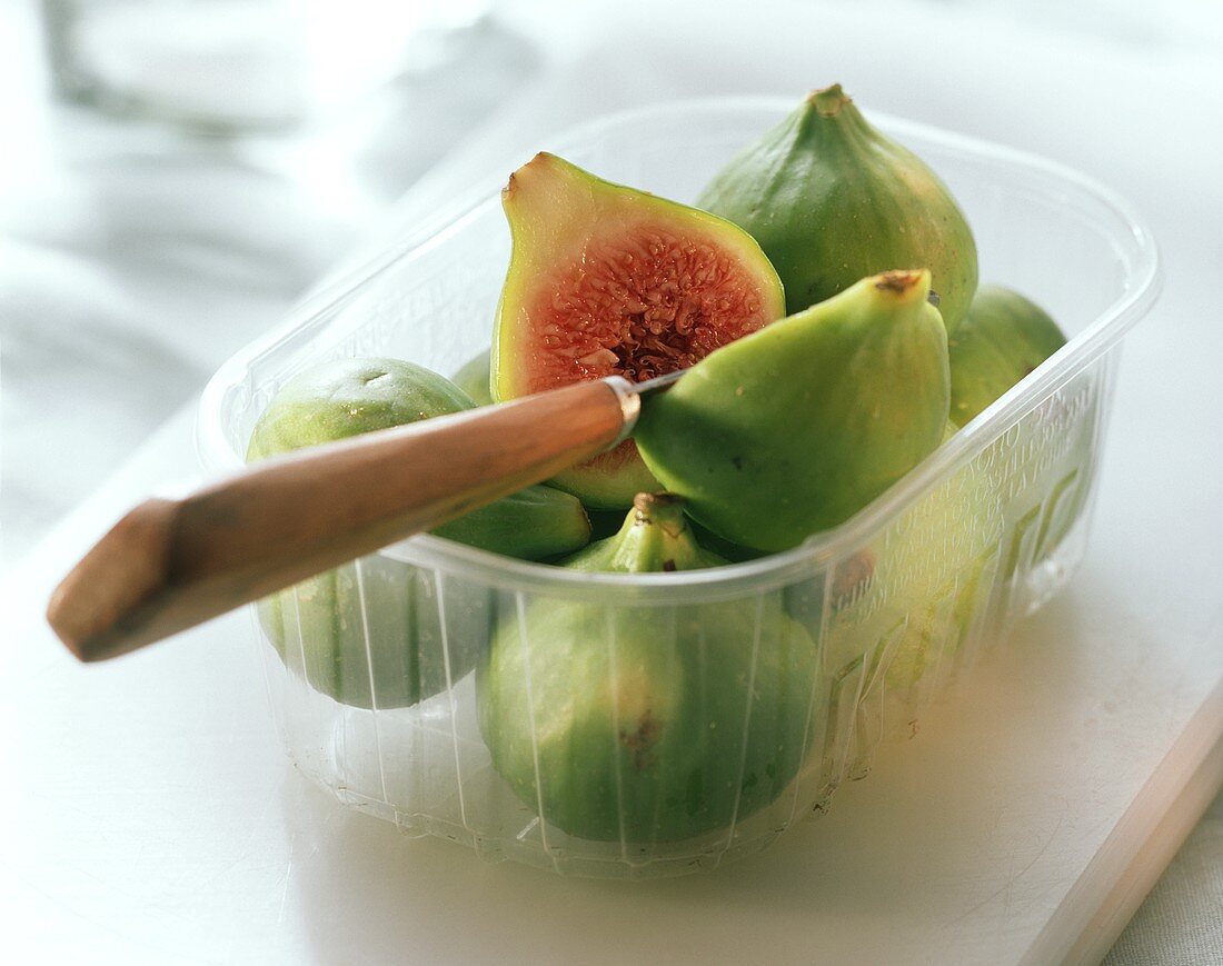 Green figs, one halved with knife in plastic punnet