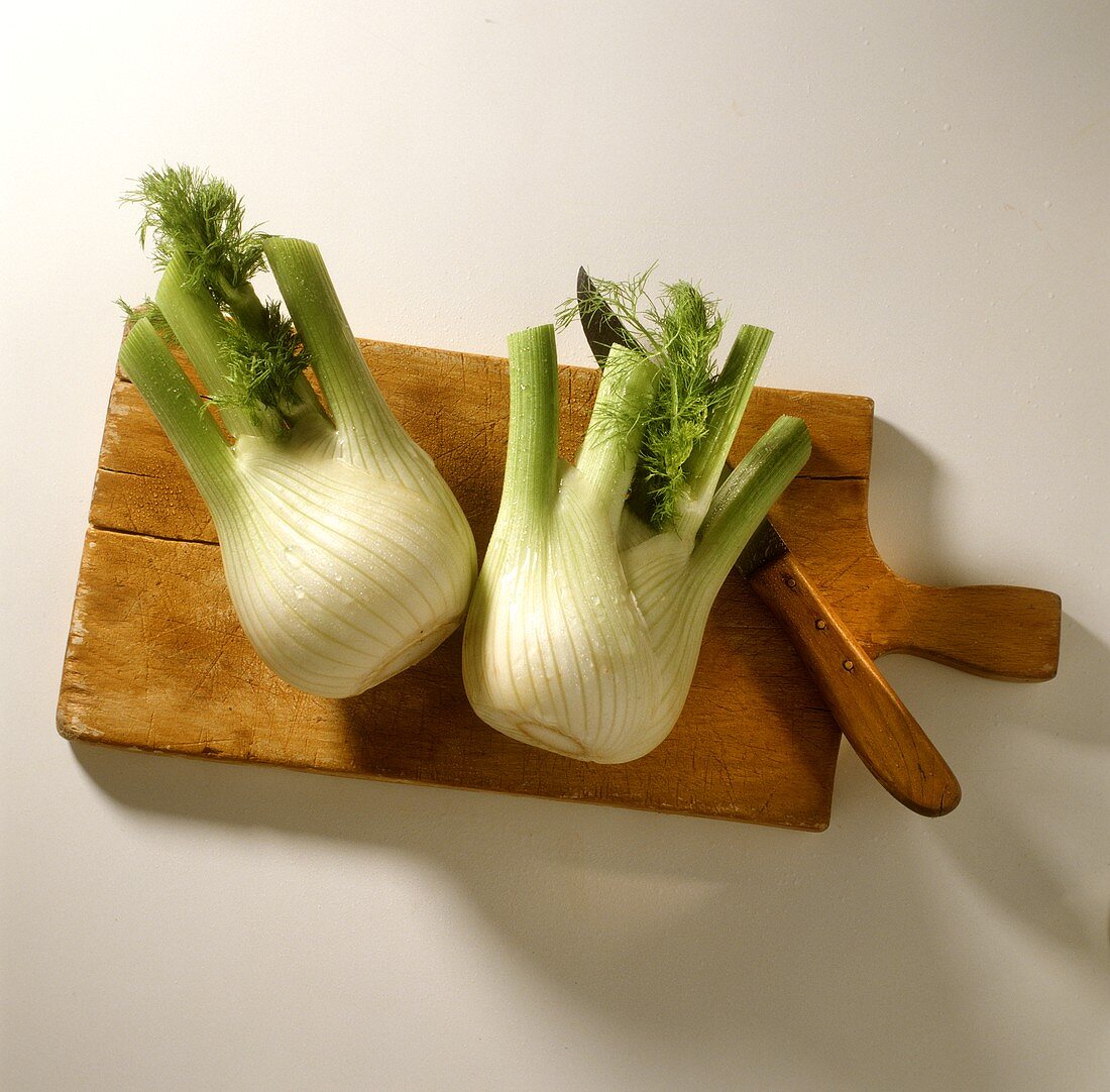 Two fresh fennel bulbs with knife on chopping board
