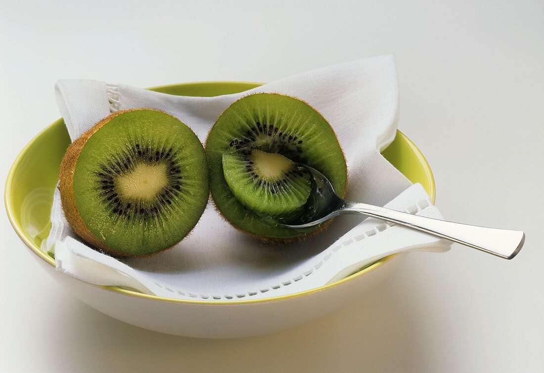 Two kiwi fruit halves with spoon on napkin in a bowl