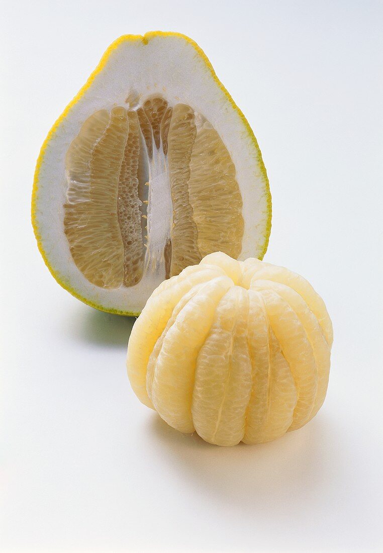 Peeled pomelo in front of halved pomelo on white background