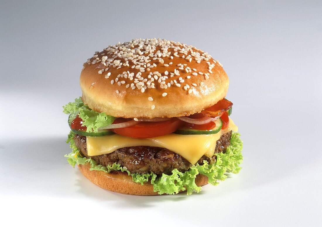 A cheeseburger with tomatoes and gherkins, light background