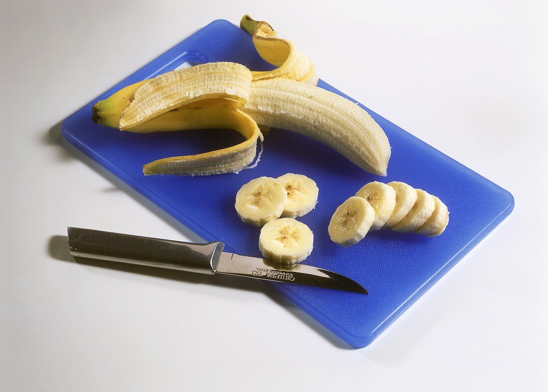 Banana, half-peeled, and banana slices on chopping board