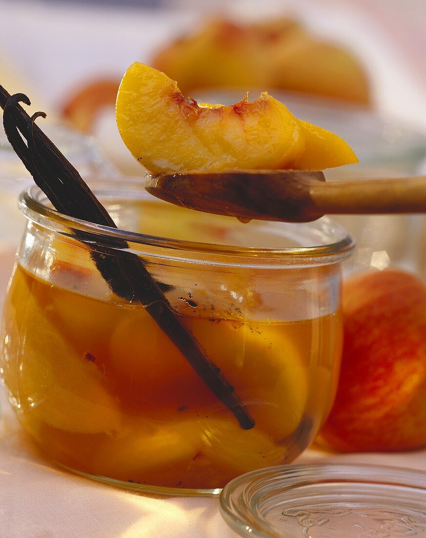 Oranges and peaches with vanilla sticks in open jar