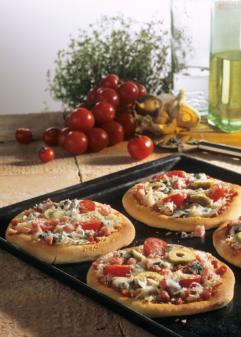 Small sauerkraut pizzas with tomatoes & olives on baking sheet