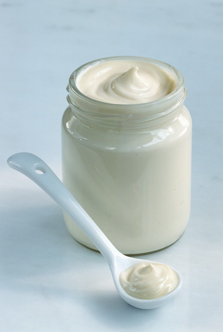 Mayonnaise in opened jar & in front of it on white spoon