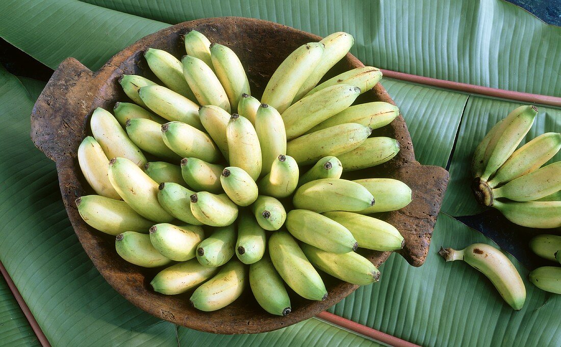 Baby bananas in a wooden bowl on banana leaf