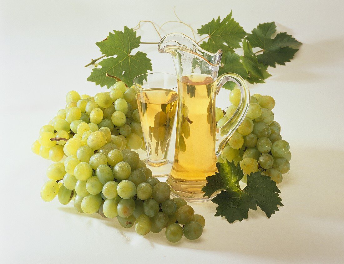 Grape juice in glass and jug surrounded by green grapes