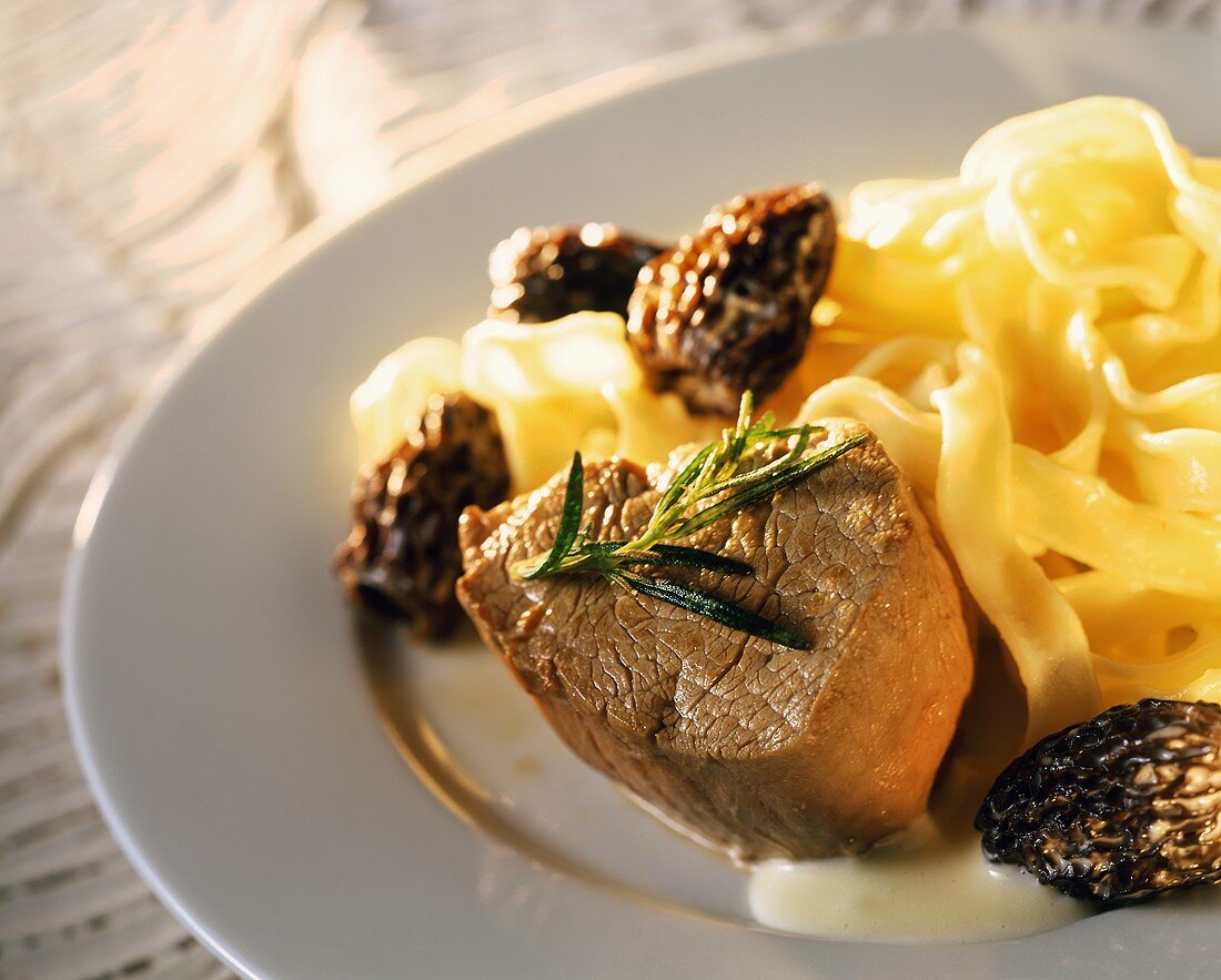 Fried veal steak with morels and ribbon pasta on plate