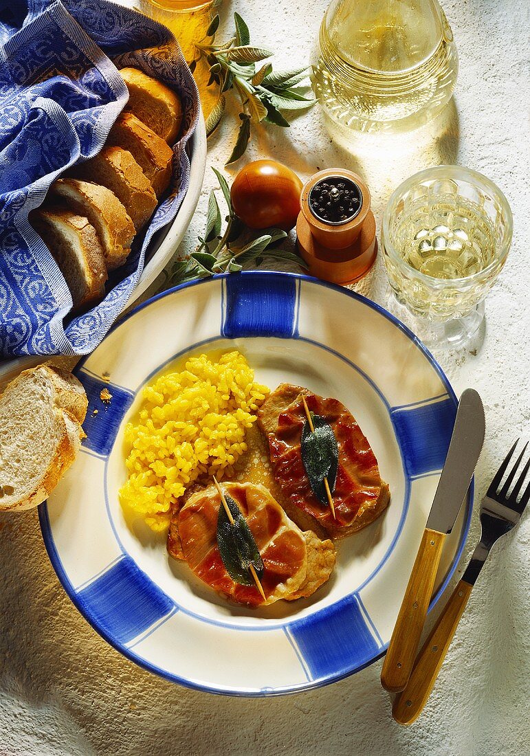 Saltimbocca mit Risotto auf blau-weißem Teller; Brot, Wein