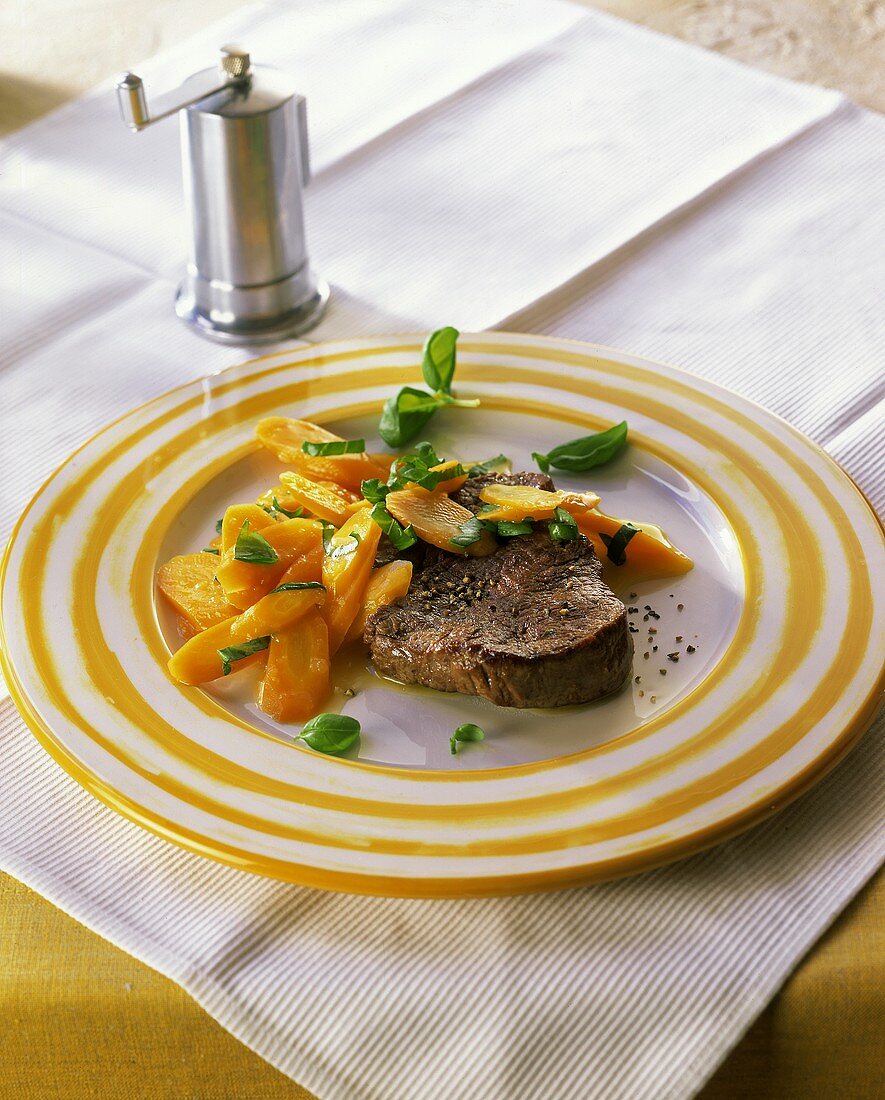 Pfeffersteak mit Möhren und frischem Basilikum auf Teller