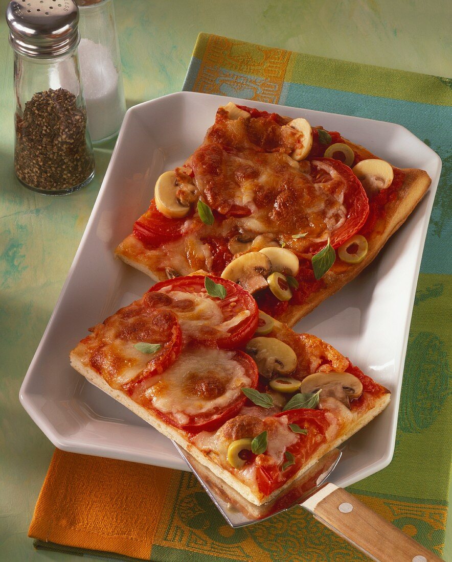 Pizza with tomatoes, olives, mushrooms on white platter