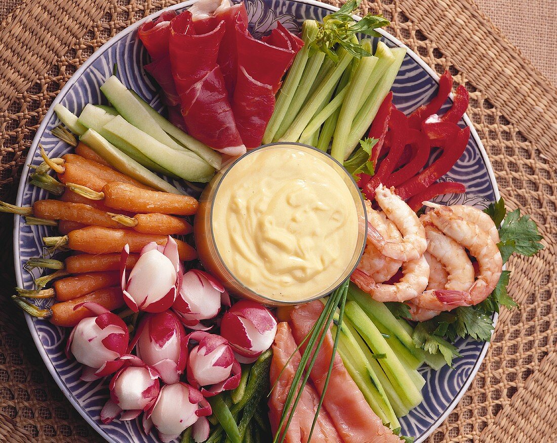 Plate of raw vegetables with shrimps, salmon, raw ham & dip